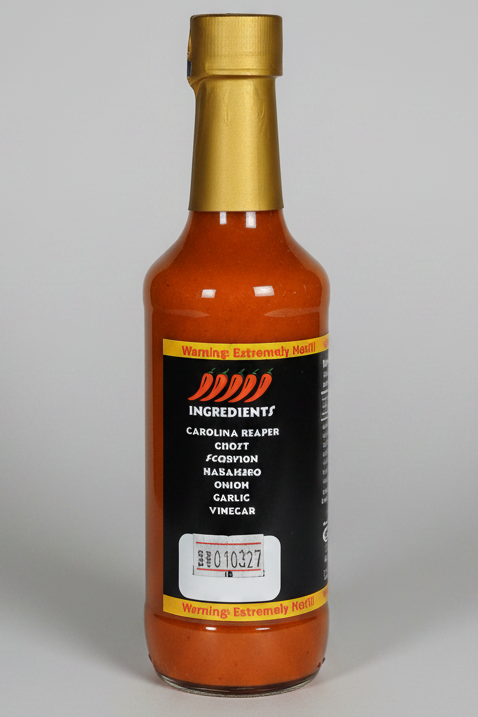 A bottle of Carolina Reaper hot sauce with a black label and gold cap, containing orange-red sauce, isolated on a white background.