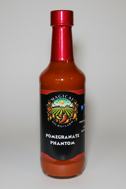 A bottle of Magical Micro Farms Pomegranate Phantom hot sauce with a metallic red cap and a black label featuring a colorful pomegranate farm illustration.